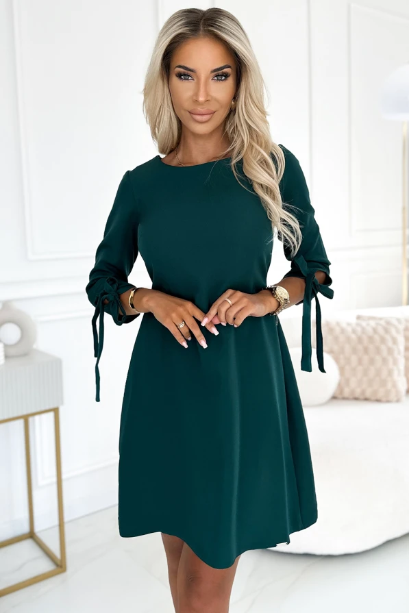Na zdjęciu znajduje się elegancka sukienka trapezowa Alice w głębokim zielonym kolorze, z ozdobnymi wiązaniami na rękawach. Sukienka Alice prezentuje się stylowo i jest idealna na różne okazje.