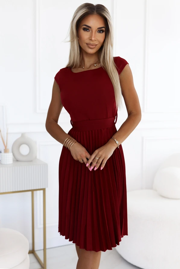 Na zdjęciu znajduje się elegancka, plisowana sukienka w kolorze bordowym, która idealnie podkreśla sylwetkę. Sukienka plisowana ma klasyczny krój z krótkimi rękawami, co czyni ją doskonałym wyborem na różne okazje.