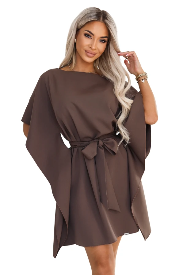 Modelka w sukience SOFIA marki Numoco w odcieniu brązu mokka. Sukienka sięga przed kolana, ma dekolt w łódkę, szerokie motylkowe rękawy i pasek zawiązany w talii na kokardę.